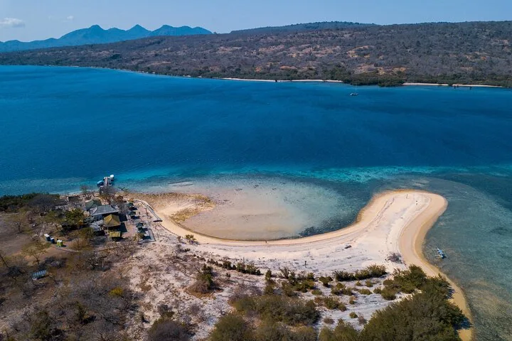 An aerial view of Menjangan Island with a beach, structures, and surrounding water.