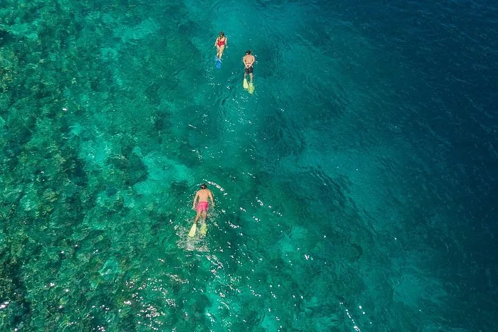 Three people snorkeling in clear, bright turquoise water.